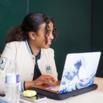 student in white coat working on a laptop